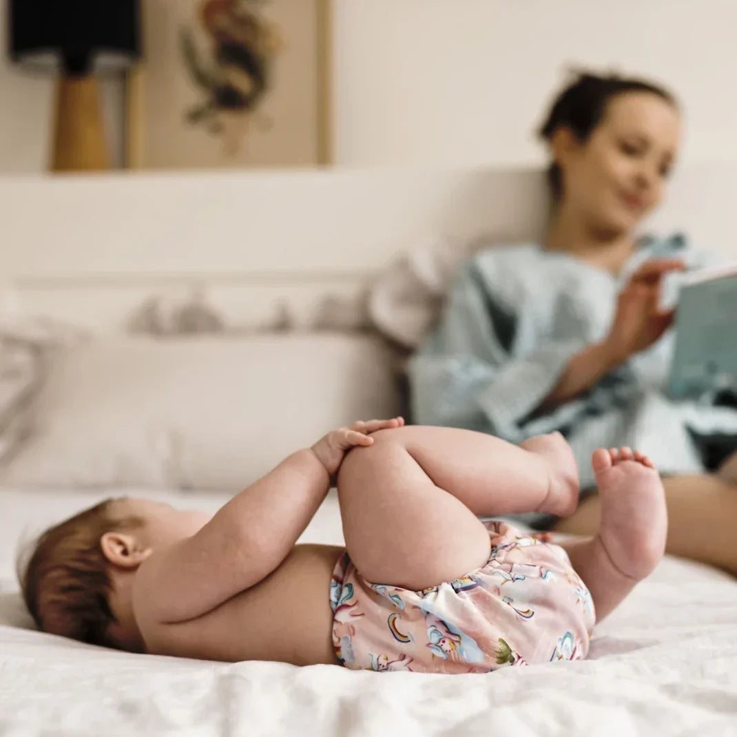 Baby ligt op bed met wasbaar oefenbroekje terwijl mama leest