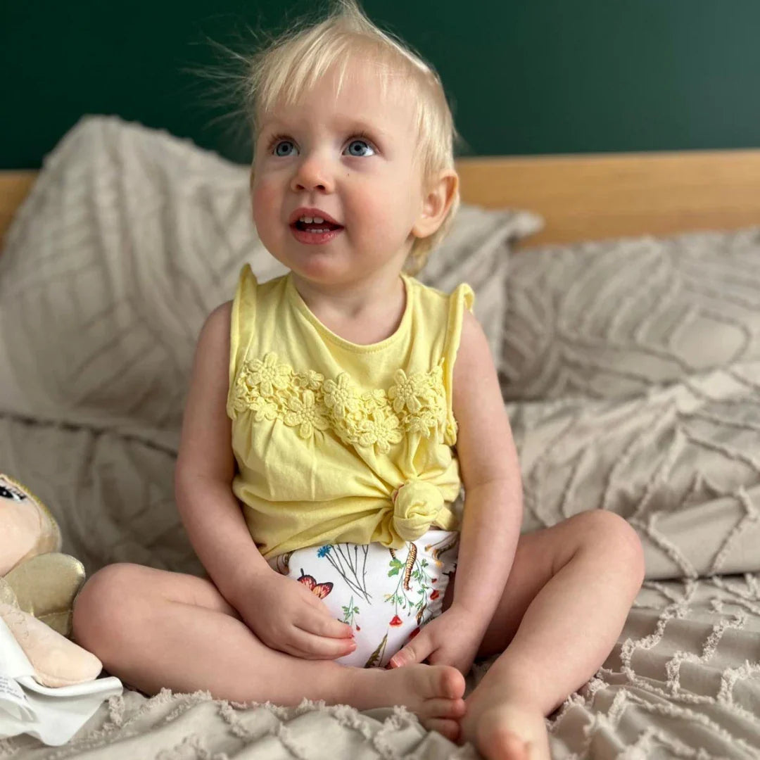 Meisje zit op bed met wasbaar zindelijkheidsbroekje met bloemen