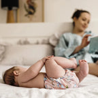 Baby met wasbaar oefenbroekje met eenhoorns, mama op de achtergrond