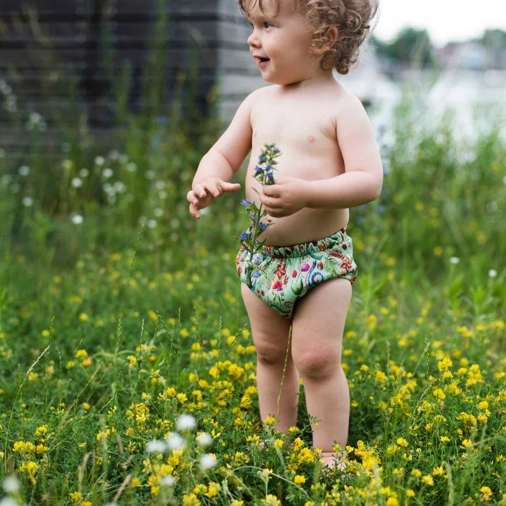 Peuter met krullen in het gras met wasbare oefenbroekjes met bloemen